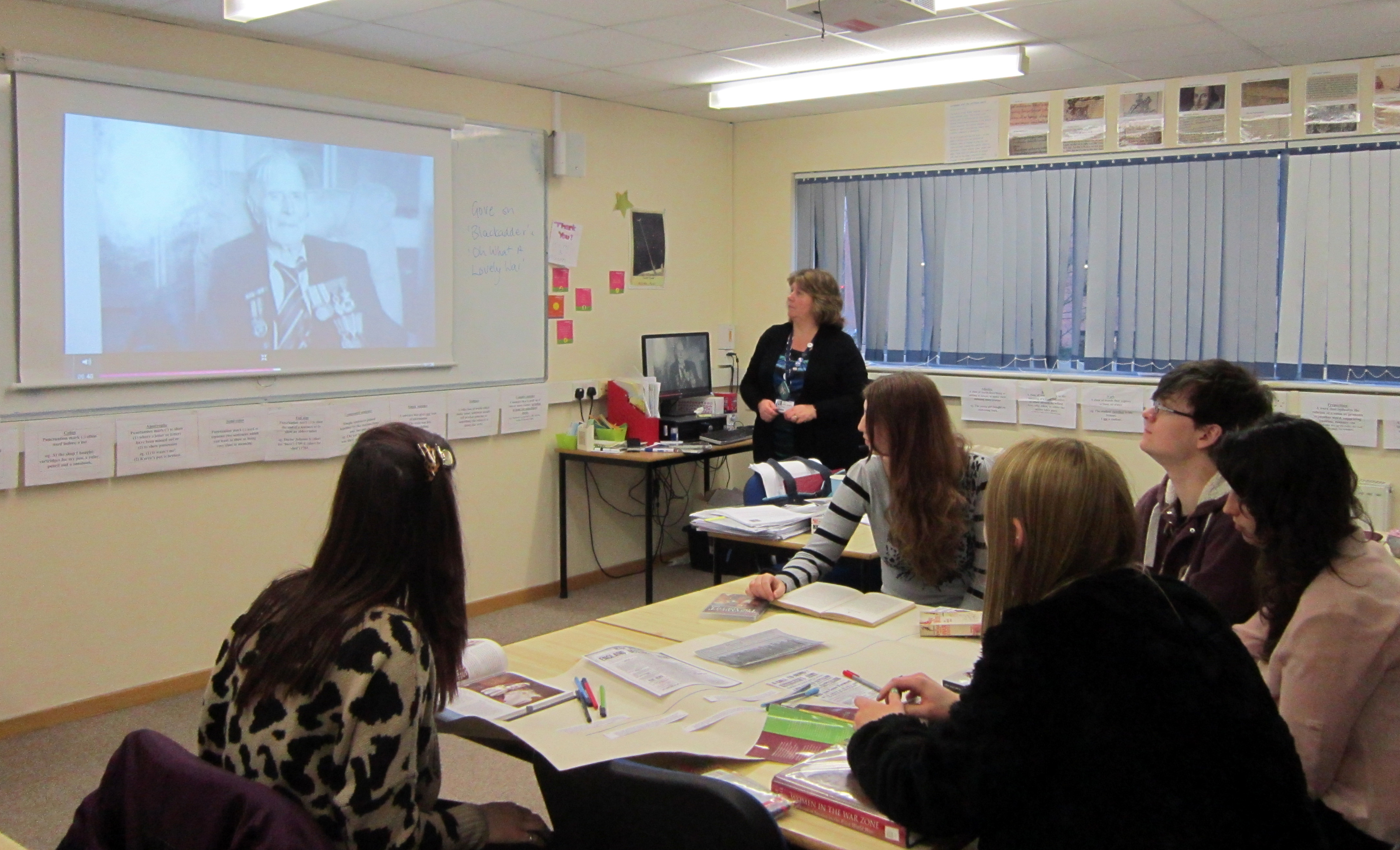 Pupils in classroom watch as teacher presents something on the interactive whiteboard.