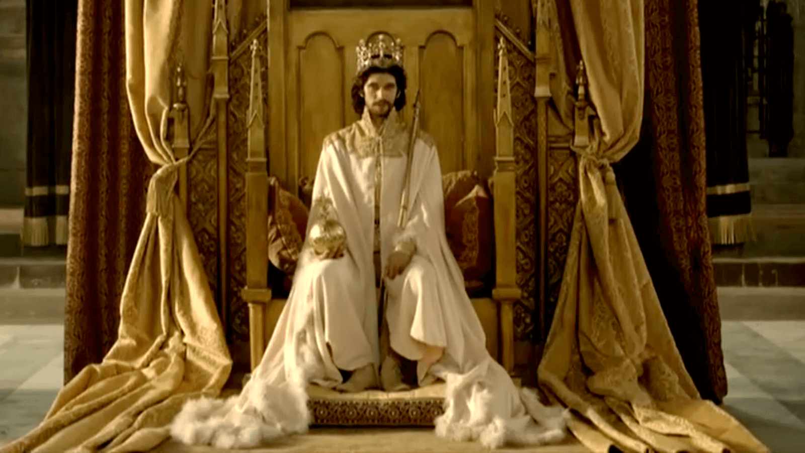 Still from Richard 2nd. King sits on throne with crown covered in furs.