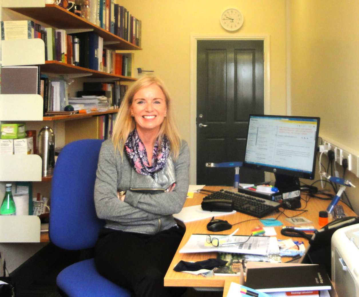 Female teacher sits at desk in office surrounded by bookshelves