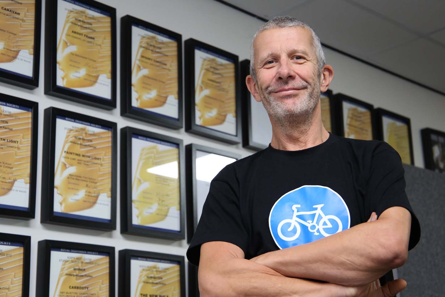 Male teacher smiles next to walls of awards