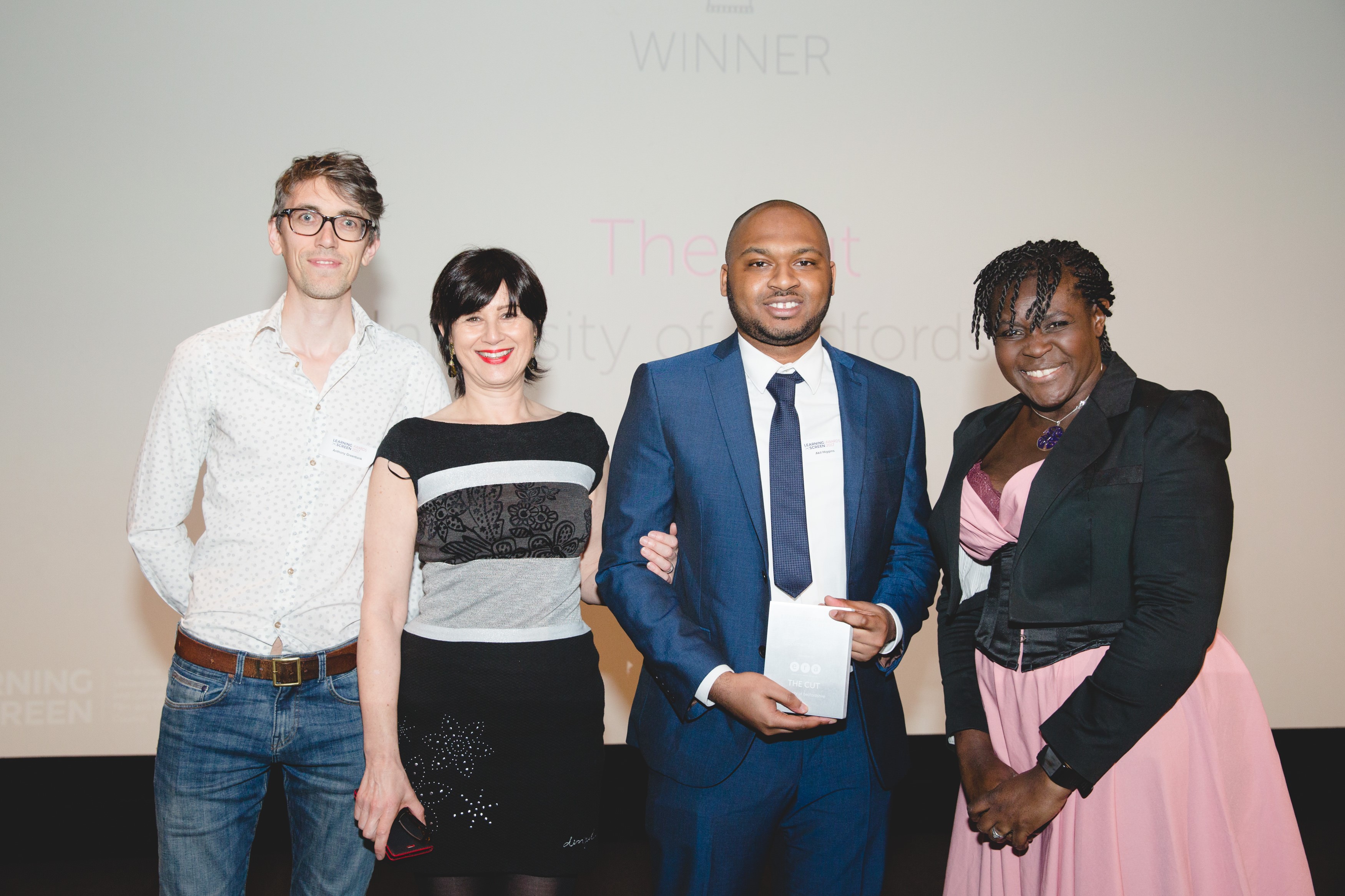 Four people line up at awards ceremony one is holding the award