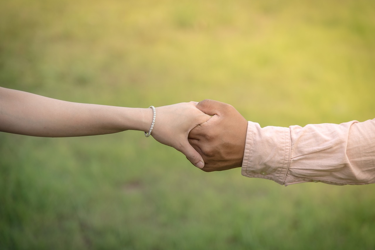 An ethnically diverse couple holds hands. Grass is in the background