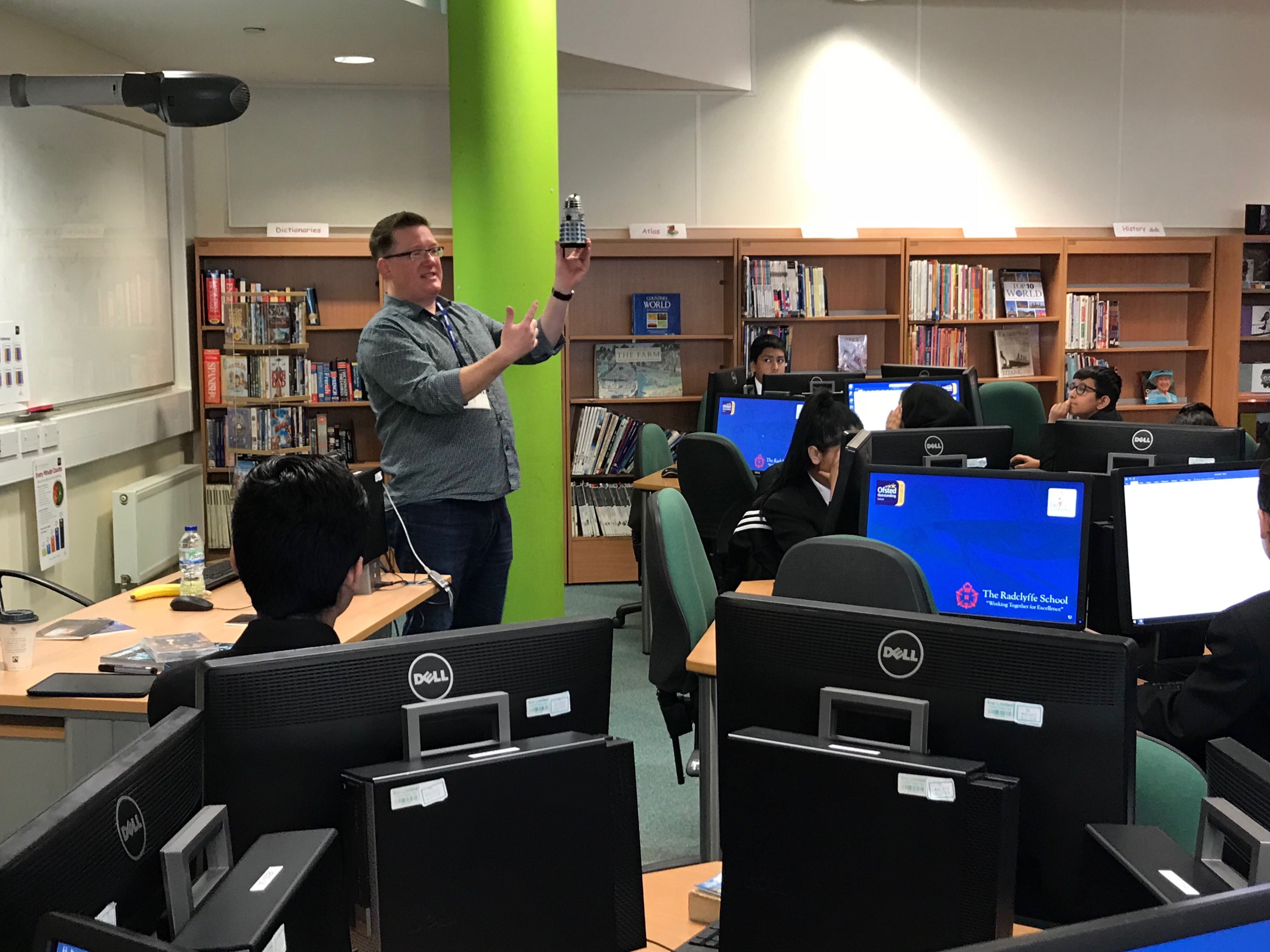 Teacher holds up a doctor who dalek to a room full of students.