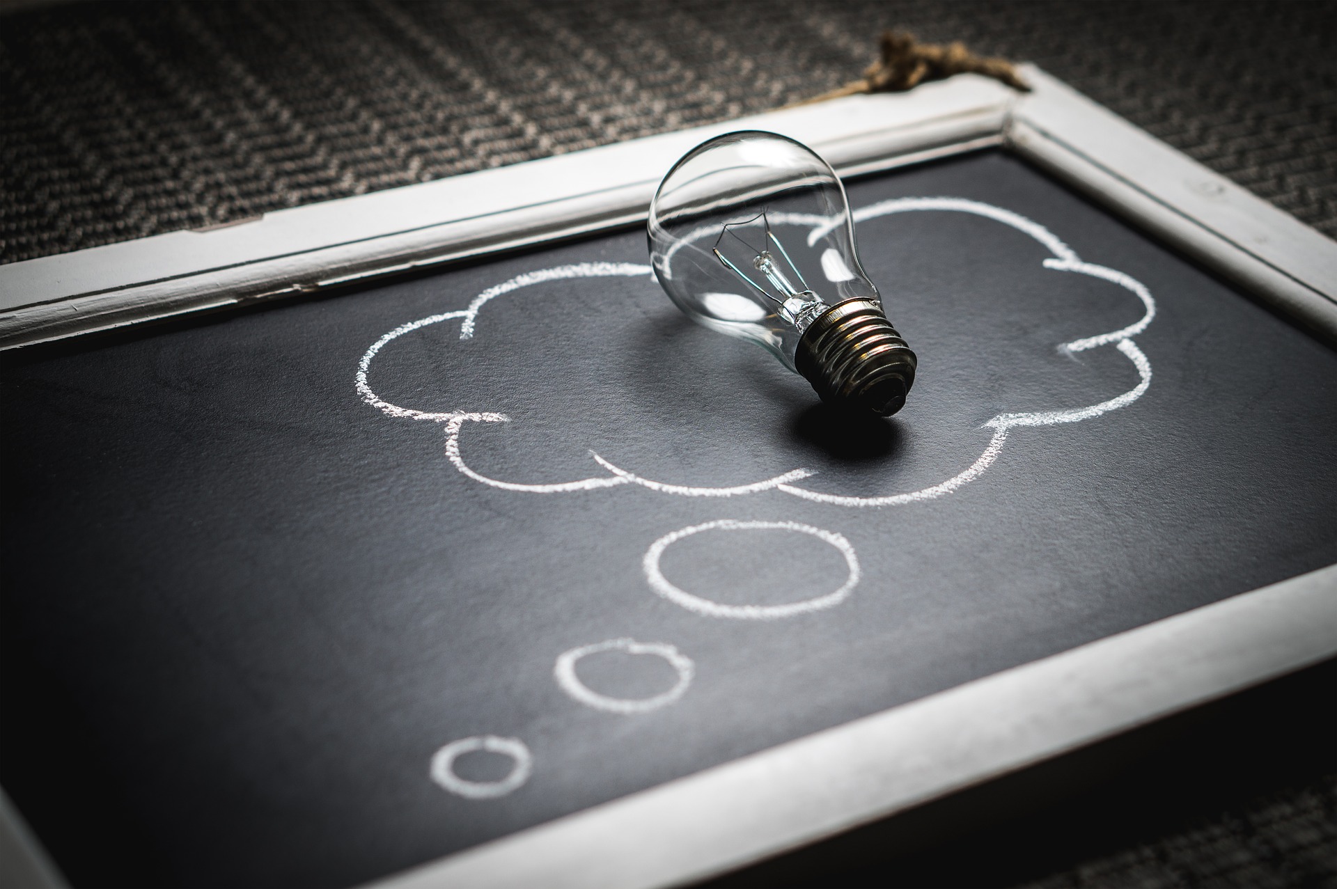 A light bulb placed on top of a blackboard with a thought bubble drawn in chalk