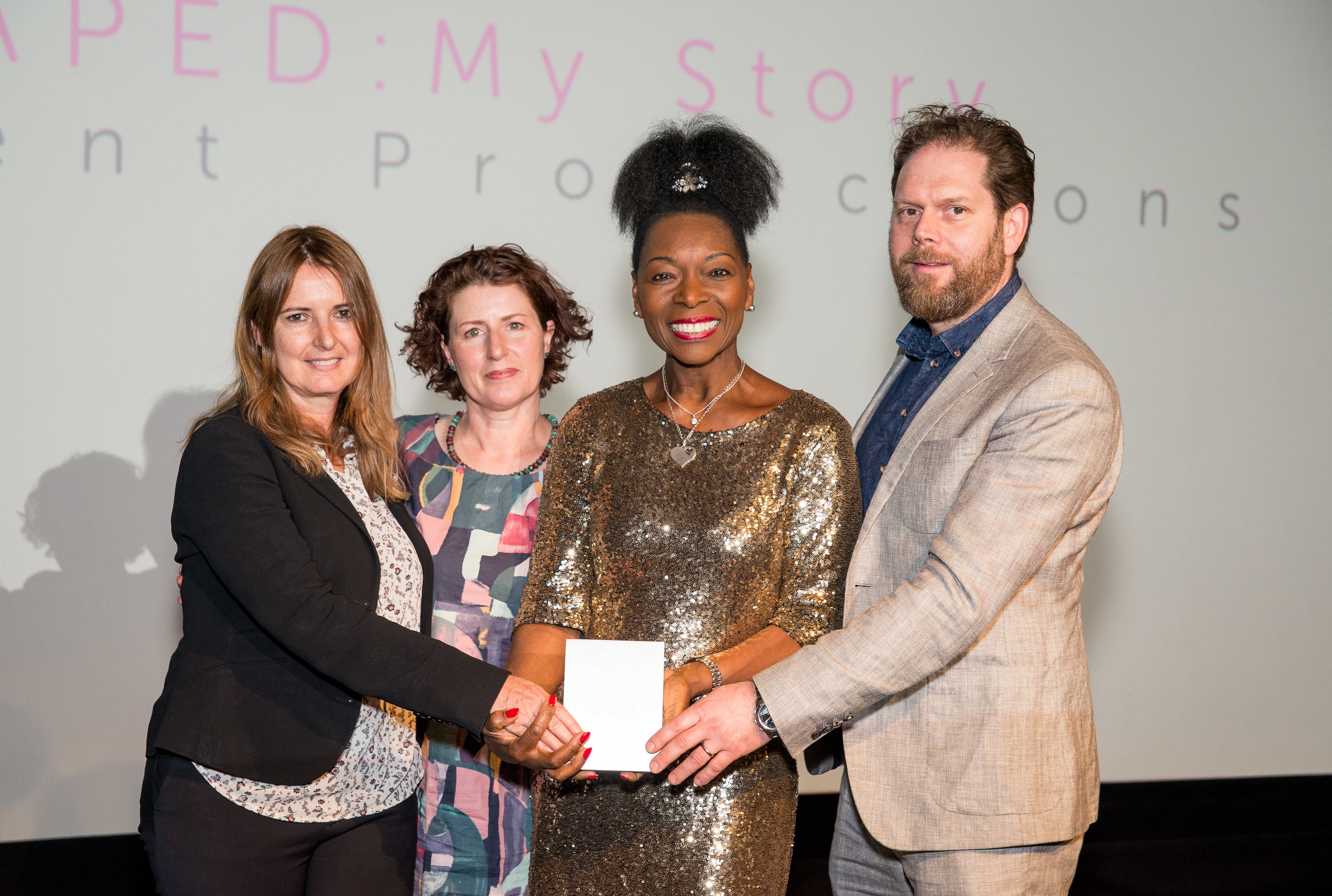 three women and one man hold an award at an award ceremony