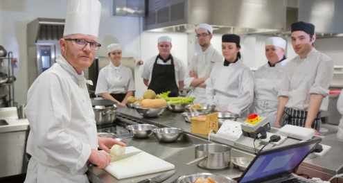 A Group of chefs in uniforms stand around a kitchen ready to work