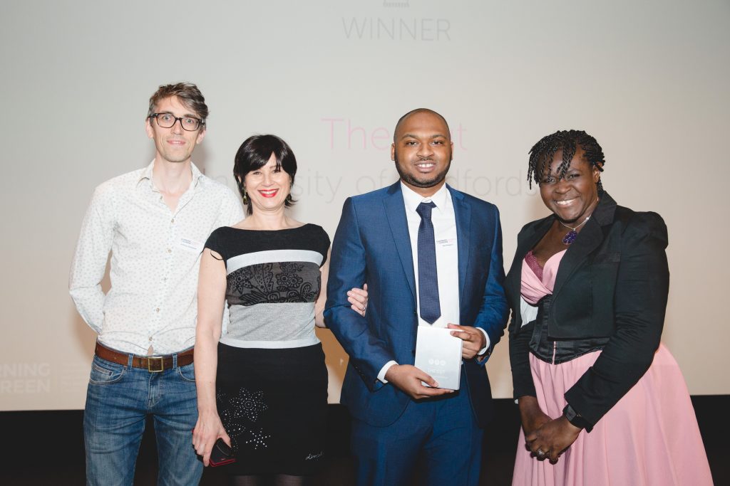 Four people stand in a row at an awards ceremony. One holds an award